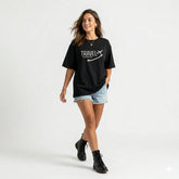 Woman wearing a black t-shirt with 'Travel is my Therapy' text and airplane graphic on a gradient background