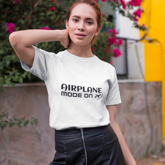 Woman wearing a white t-shirt with 'Airplane Mode On' text, standing outdoors with flowers in the background.