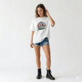 Woman wearing a white t-shirt with a graphic design and denim shorts on a white background