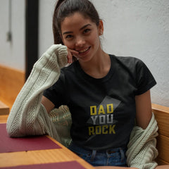 Woman wearing a black t-shirt with 'DAD YOU ROCK' text, sitting indoors.