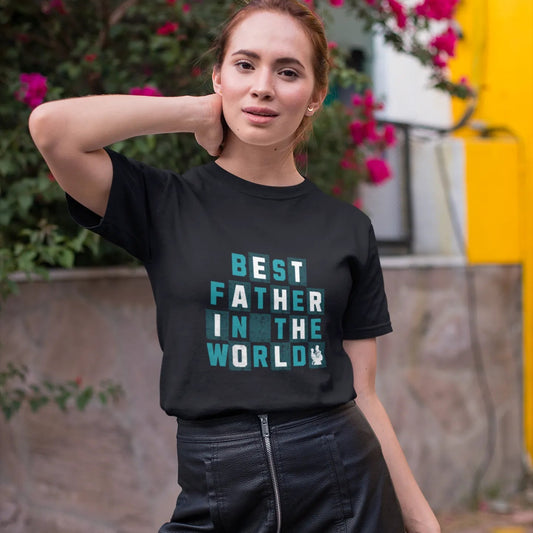Woman wearing a black t-shirt with 'Best Father in the World' text, standing outdoors with flowers in the background.