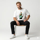 Man sitting on a chair wearing a white t-shirt with a graphic design, black pants, and white sneakers.