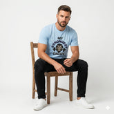 Man sitting on a wooden chair wearing a light blue t-shirt with text and graphics.