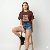 Woman wearing a maroon t-shirt with text, holding a coffee cup outdoors.