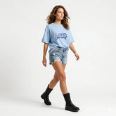 Woman wearing a light blue 'Love yourself' t-shirt, denim shorts, and black boots on a white background