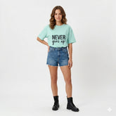 Woman wearing a light blue t-shirt with 'Never Give Up' text, denim shorts, and black boots on a white background