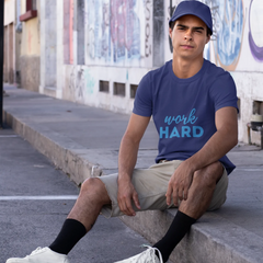 Man sitting on a street corner wearing a blue t-shirt with 'work HARD' text.