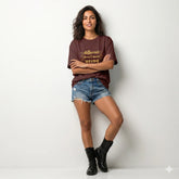 Woman wearing a brown t-shirt with text, denim shorts, and black boots on a white background