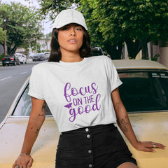 Person wearing a white t-shirt with 'focus on the good' text, standing next to a yellow car on a street.