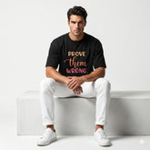 Man wearing a black t-shirt with 'Prove Them Wrong' text, sitting on a white bench.