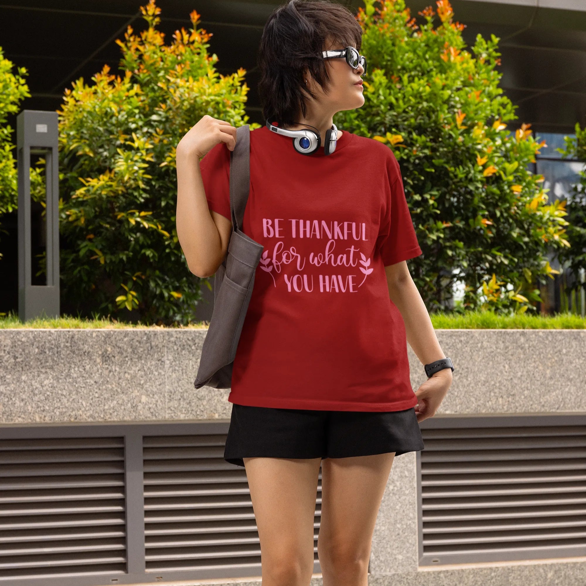 Person wearing a red t-shirt with text, black shorts, and black boots standing outdoors.