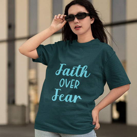 Woman wearing a teal t-shirt with 'Faith Over Fear' text outdoors.