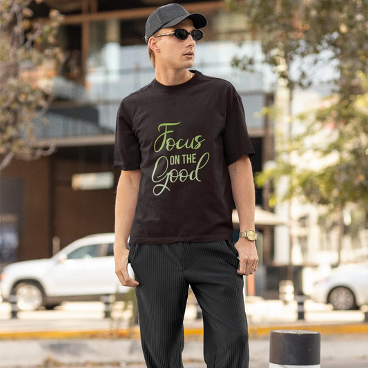 Man wearing a black t-shirt with 'Focus on the Good' text, standing on a street.