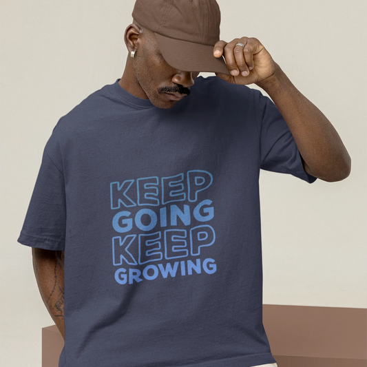 Man wearing a navy t-shirt with 'KEEP GOING KEEP GROWING' text and a brown cap.