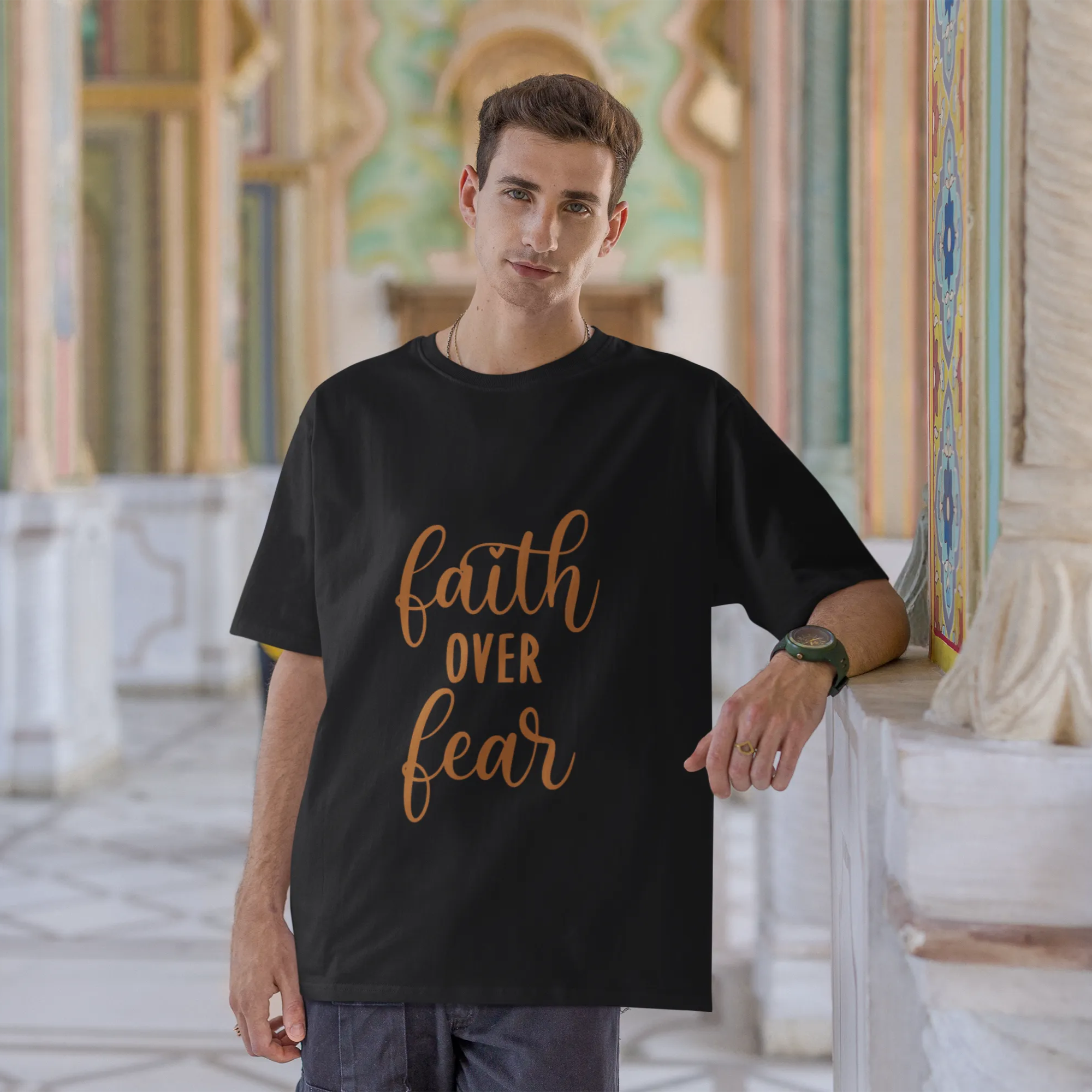 Man wearing a black t-shirt with 'faith over fear' text in an ornate architectural setting.