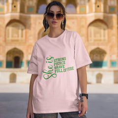 Woman wearing a pink t-shirt with green text in front of an architectural building.