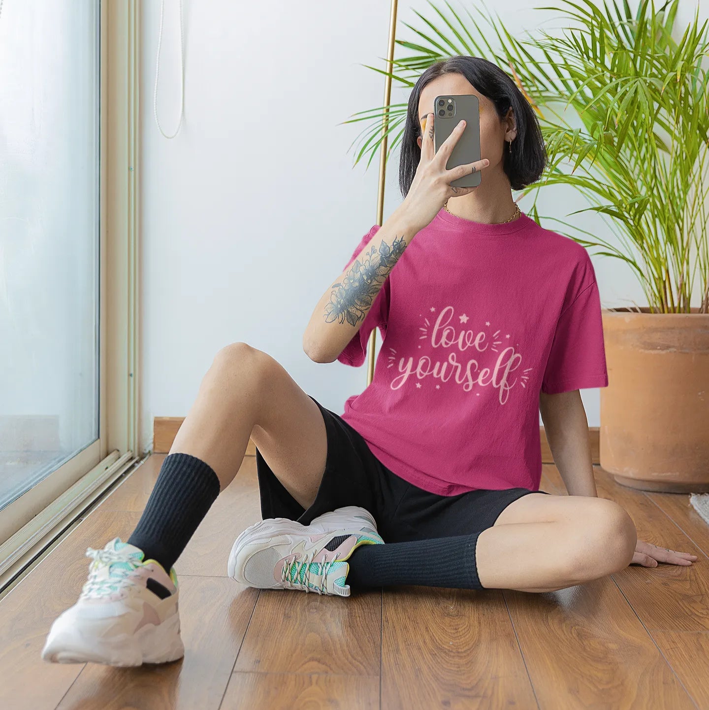 Person wearing a pink t-shirt with 'live yourself' text, sitting on the floor indoors.