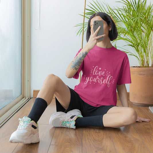 Person wearing a pink t-shirt with 'live yourself' text, sitting on the floor indoors.