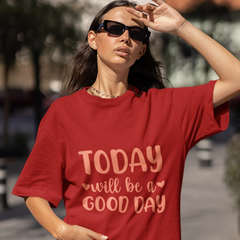 Woman wearing a red t-shirt with 'Today will be a good day' text outdoors.