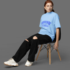 Person wearing a light blue t-shirt with text, sitting on a chair against a gray background