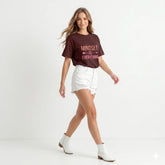 Woman wearing a brown t-shirt with 'Mindset is Everything' text, white shorts, and white boots on a light gray background