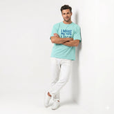 Man wearing a light blue t-shirt with text and white pants on a white background