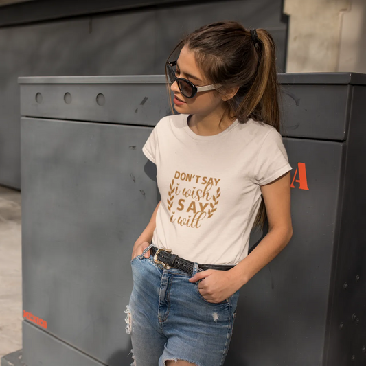 Woman wearing a white t-shirt with text and ripped jeans standing next to a gray wall.