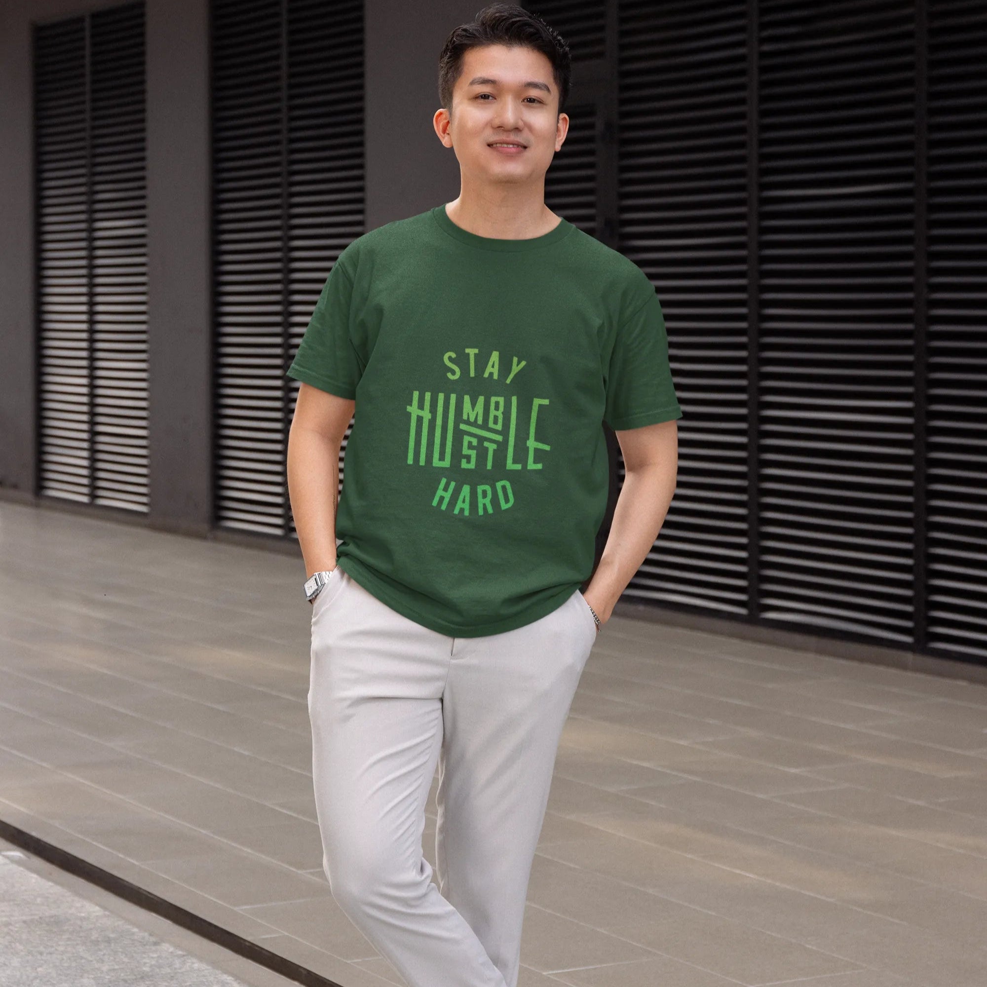 Man wearing a green t-shirt with text, standing outdoors on a pavement.