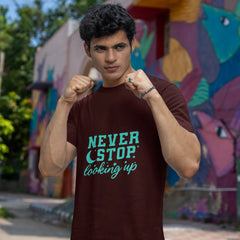 Person wearing a t-shirt with 'Never Stop Looking Up' text in front of a colorful mural.