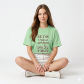 Woman wearing a light green t-shirt with a motivational quote against a geometric-patterned wall.