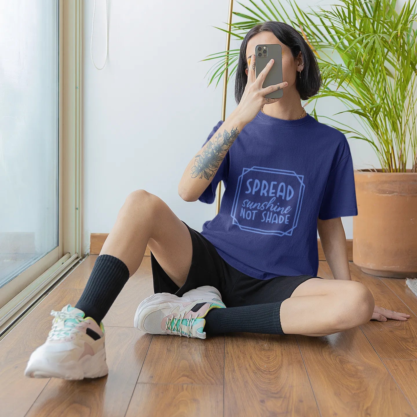 Person sitting on the floor taking a mirror selfie wearing a blue t-shirt with text.
