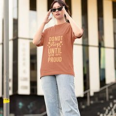 Person wearing a brown t-shirt with motivational text, standing outdoors.