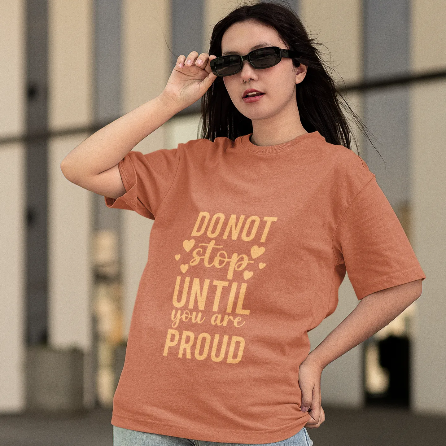 Woman wearing a brown t-shirt with motivational text, standing outdoors.