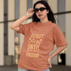 Woman wearing a brown t-shirt with motivational text, standing outdoors.