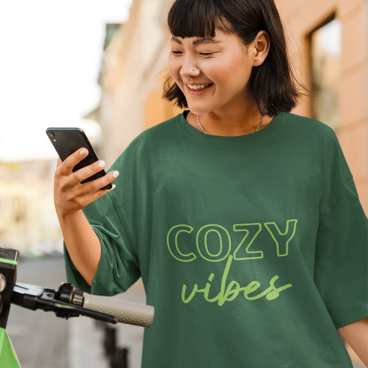 Woman in a green 'Cozy Vibes' shirt using a smartphone outdoors.