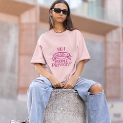 Person wearing a pink t-shirt with text and ripped jeans sitting on a concrete block outdoors.
