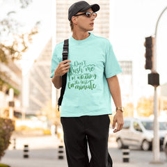 Person wearing a light blue t-shirt with text, black pants, and a cap in an urban setting.