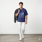 Man wearing a blue t-shirt with text, white pants, and a gray jacket against a white background