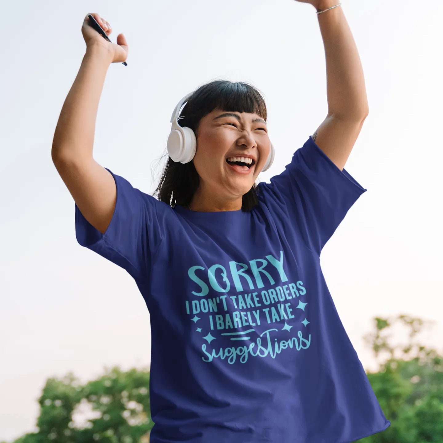 Person wearing a blue t-shirt with text, standing outdoors with arms raised.