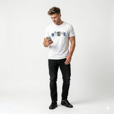 Man wearing a white t-shirt with 'BRAVE' printed on it, standing against a plain background.
