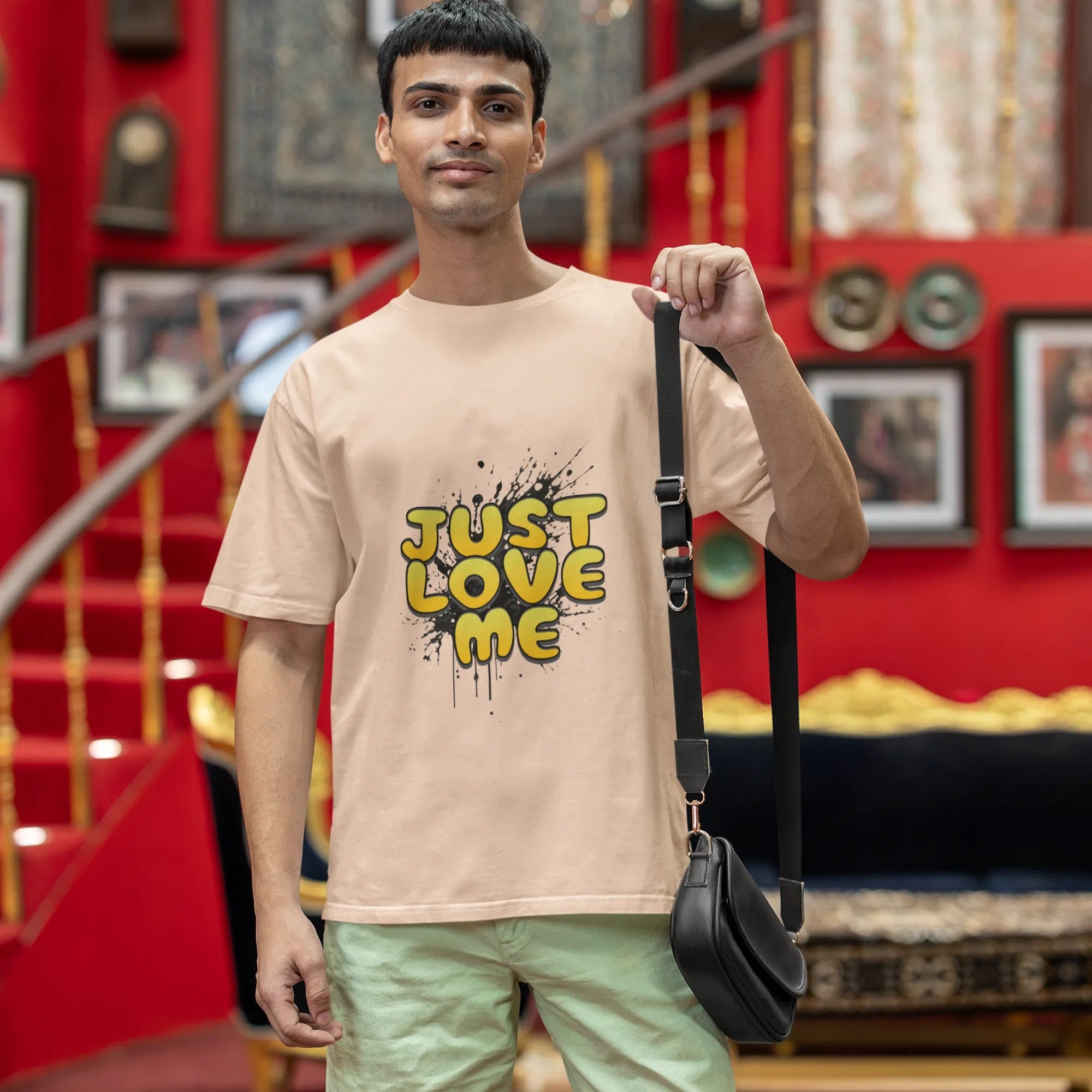 Man wearing a beige t-shirt with 'Just Love Me' text and green shorts, standing in a decorated room.