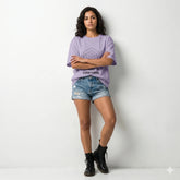Woman wearing a light purple t-shirt with text, beige skirt, and white sneakers on a light purple background
