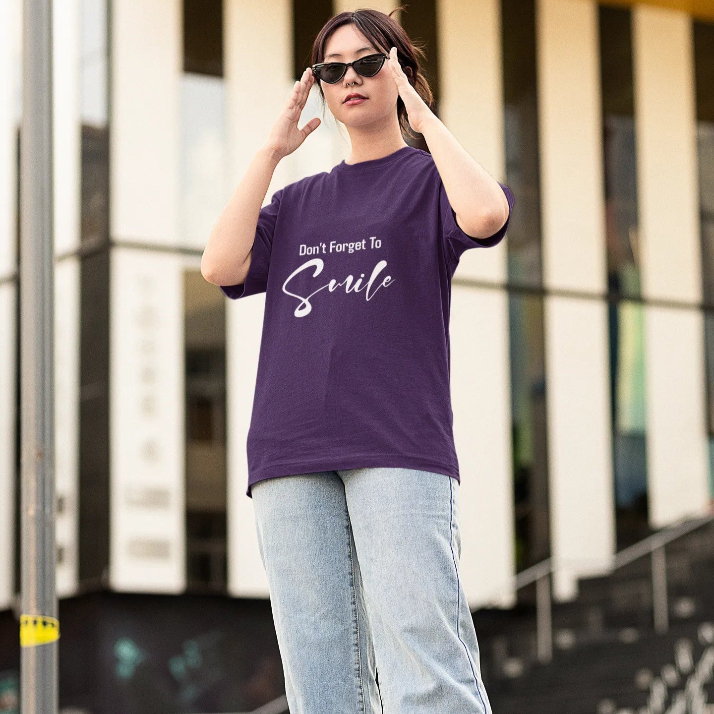 Person wearing a purple t-shirt with text and light blue jeans standing outdoors.