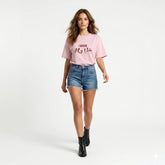 Woman wearing a pink t-shirt with text, sitting on a black stool against a red background