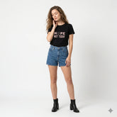 Woman wearing a black t-shirt with text and blue shorts on a white background