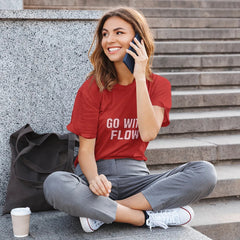 Woman sitting on steps talking on a phone with a red shirt and gray pants.