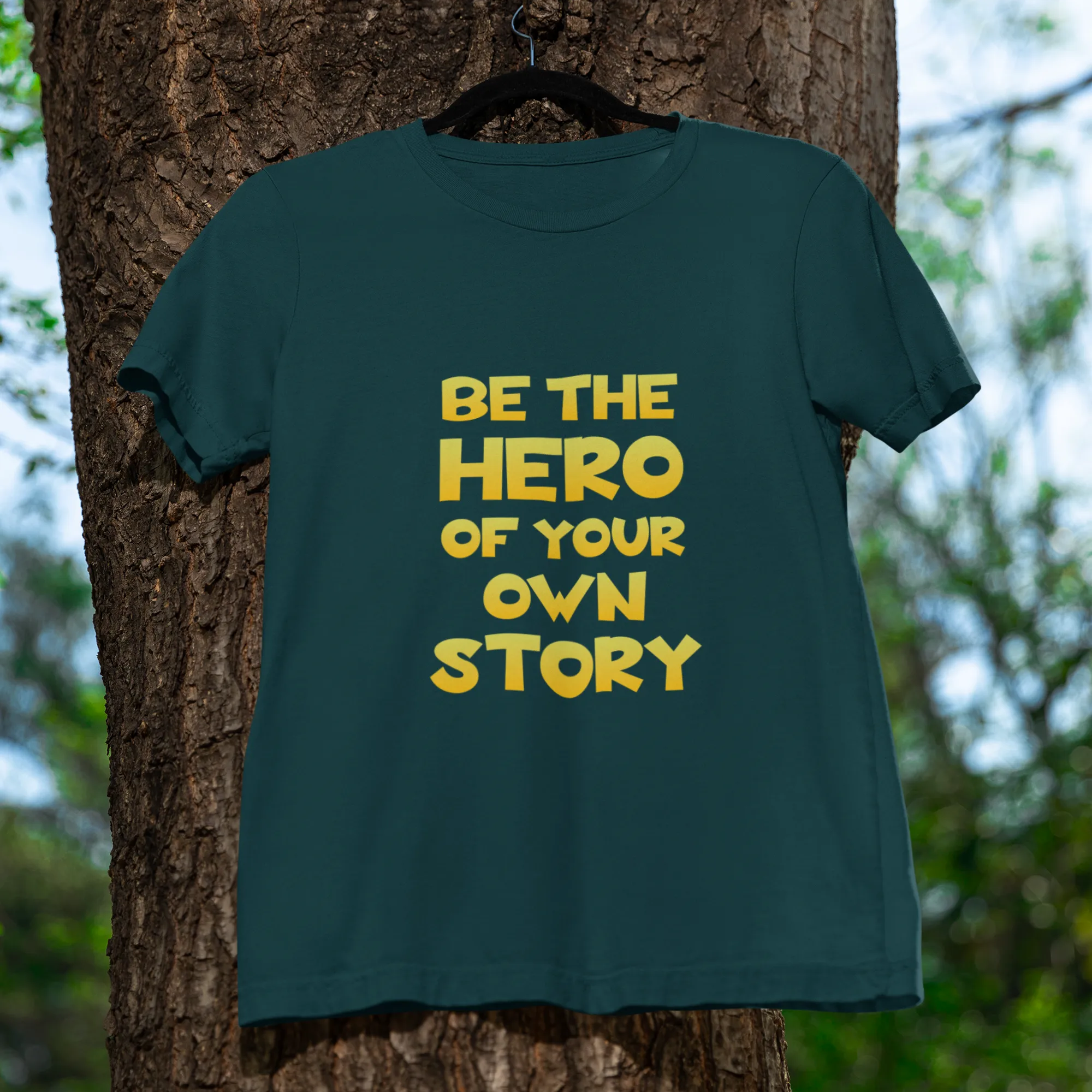Green t-shirt with 'Be the Hero of your Own Story' text on a tree