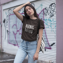 Woman wearing a brown t-shirt with 'Normal is Boring' text in front of a graffiti-covered wall.
