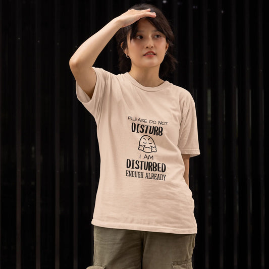 Person wearing a beige t-shirt with text and graphics, standing against a dark background