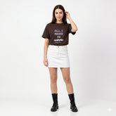 Woman wearing a brown t-shirt with text and a white skirt on a white background